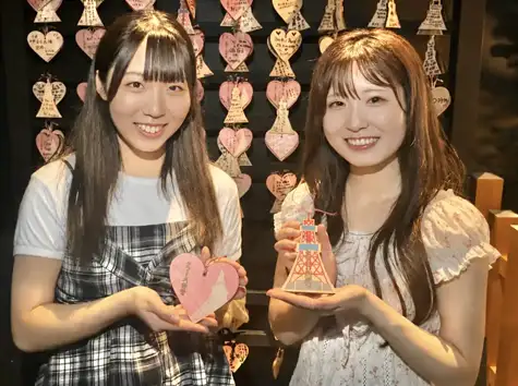 Two women smiling as they hold heart-shaped and Tokyo Tower-shaped ema plaques