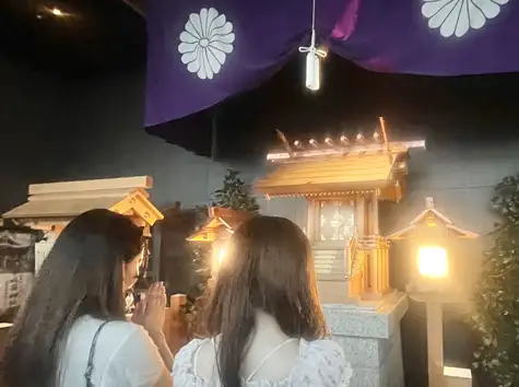 Two women seen from behind, pressing their hands together in prayer before the Tower Daijingu Shrine sanctuary