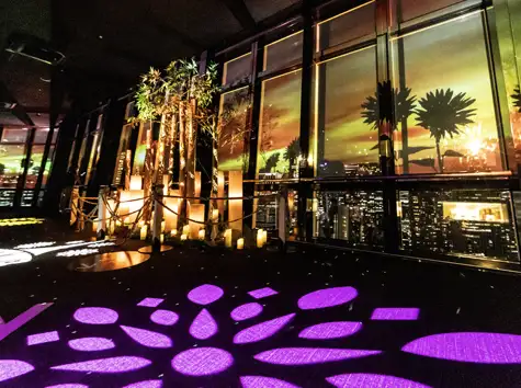 The Main Deck at dusk, with purple and yellow floral-patterned projection mapping lighting up the floor and windows
