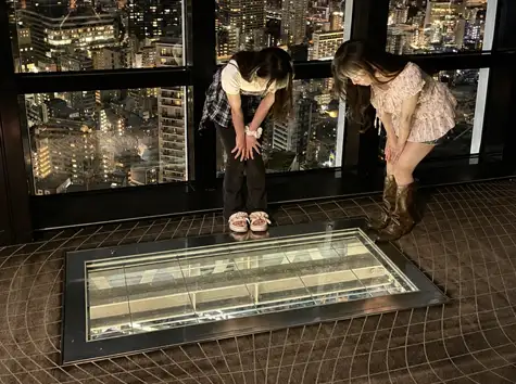 Two women peering down through the glass-floored Skywalk Window at the night view below