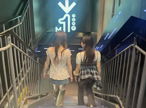 Two women seen from behind, walking down the stairs together from the Main Deck's 2nd floor to the 1st floor