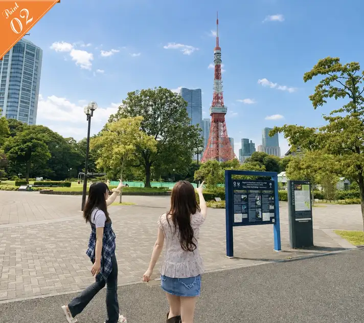 Two women seen from behind, pointing excitedly at Tokyo Tower from a path in Shiba Park