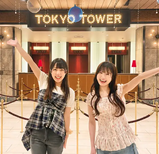 Two women striking a joyful pose in front of the glowing TOKYO TOWER sign