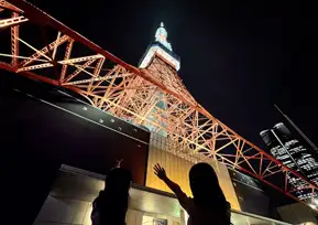 The silhouettes of two women waving as they look up at Tokyo Tower lit up in orange