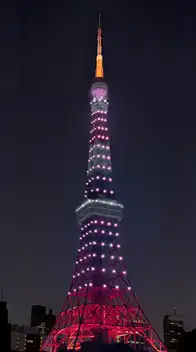 Tokyo Tower at night, bathed in shifting pink and purple light-up colors that change from day to day